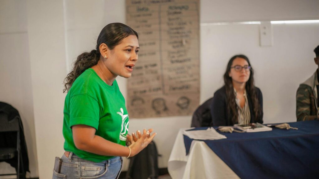 A young woman passionately speaking during an indoor meeting or workshop.