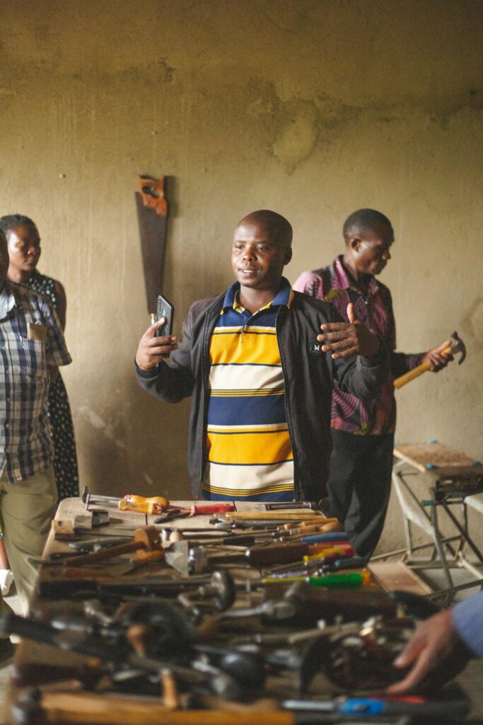 Adults engaged in a community workshop session in Kasese, Uganda surrounded by hand tools. Indoor setting.